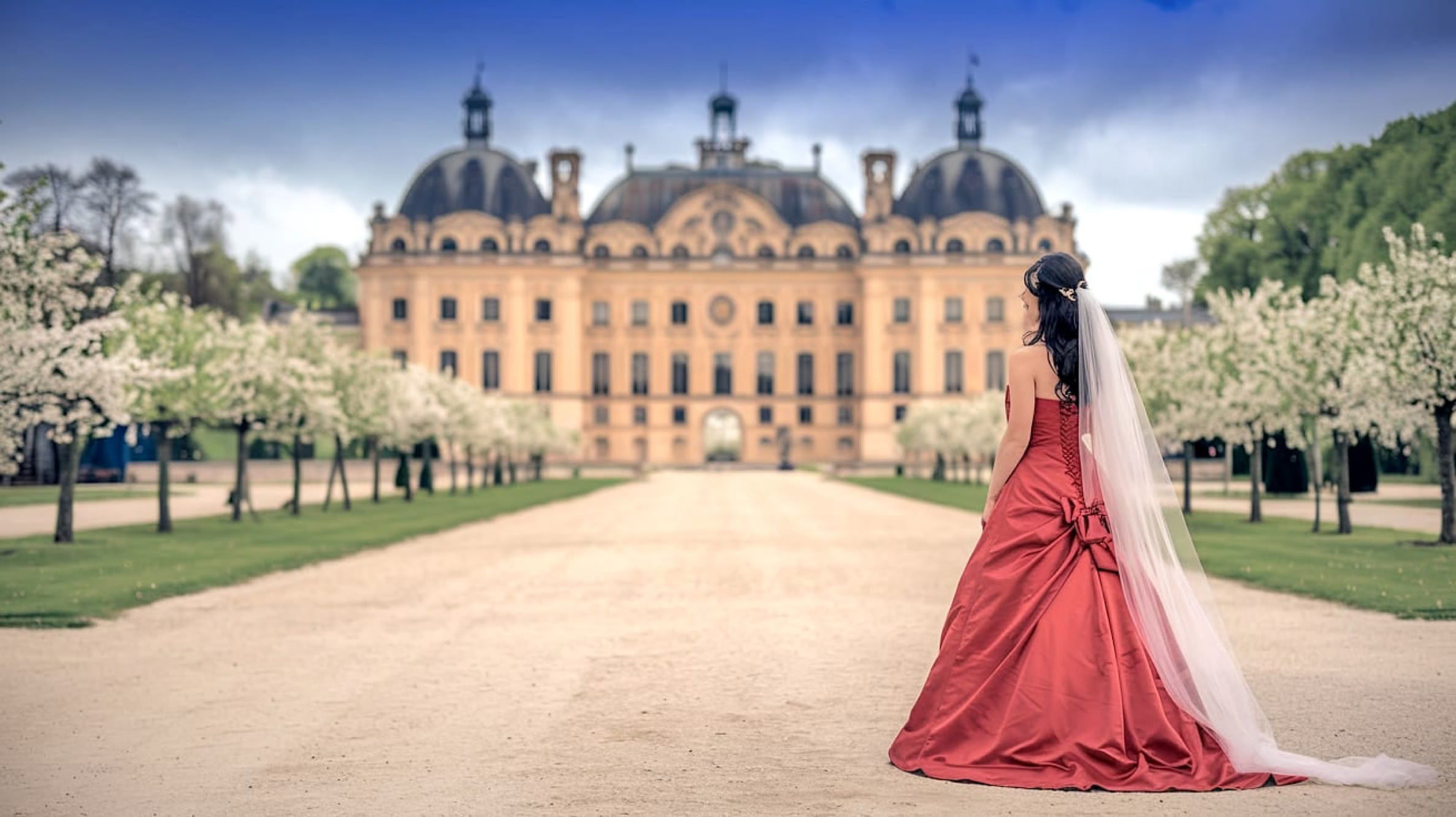 Braut im roten Hochzeitskleid vor einem Traumschloß