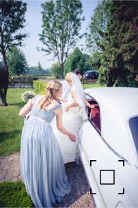 Die Trauzeugin hilft der Braut beim Einsteigen in das Hochzeitsauto